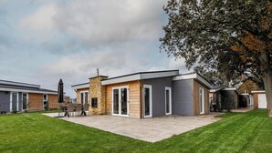 A modern residential building with a stone facade, large glass doors, and a well-maintained lawn. - Schaelsbergerbosch - Fireplace & Sauna (Bemelen)