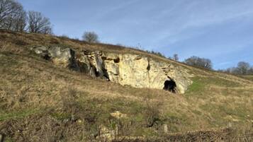 Formazione rocciosa naturale con l'ingresso di una grotta su un pendio erboso.