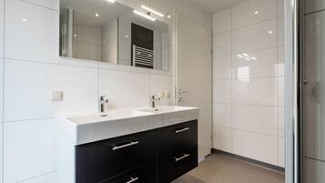 Een moderne badkamer met twee wasbakken, een grote spiegel en een douchecabine met glazen wanden.