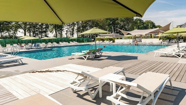 Un espace aménagé au bord de la piscine, avec des chaises longues et des parasols, une terrasse en bois et une vue dégagée sur la piscine.