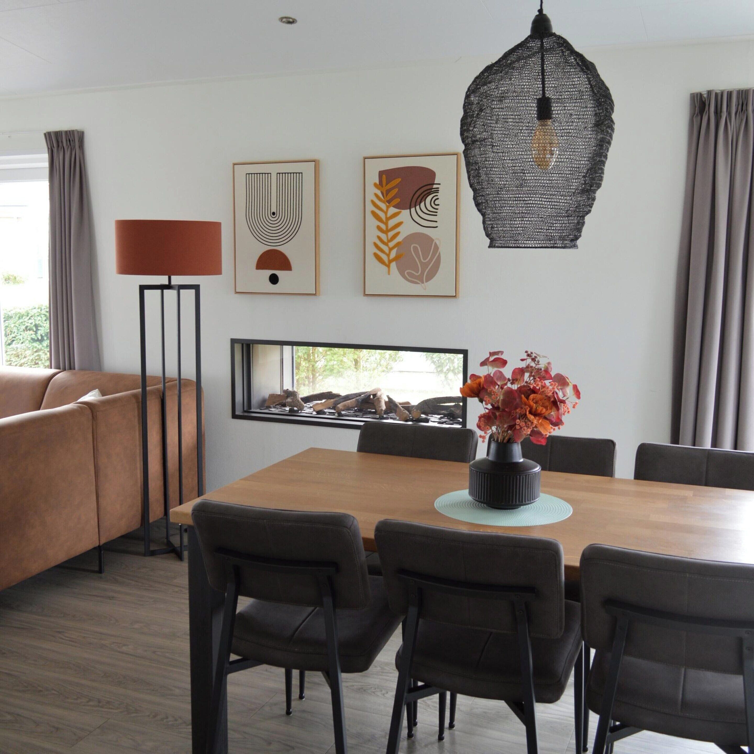 Un espace repas moderne avec une table en bois, six chaises, un vase de fleurs et des œuvres d’art accrochées au mur.