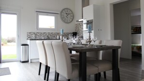 Un espace de repas moderne avec une table dressée pour quatre personnes, une horloge au mur et une cuisine en arrière-plan.