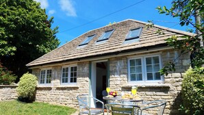 Une maison en pierre avec un toit en tuiles, un petit porche et une table avec des chaises à l’extérieur.