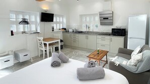 Une pièce moderne et bien éclairée, comprenant un lit, une table en bois, un canapé et un coin cuisine équipé d’un four à micro-ondes et d’un four traditionnel.
