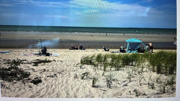 Una playa con gente, una sombrilla a rayas y una orilla arenosa.