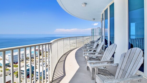 Un balcone con ringhiere bianche, sedie di legno e vista sull'oceano e sugli edifici.