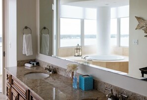 Un baño con un espejo grande, dos lavamanos y vistas a una bañera amplia a través del ventanal.