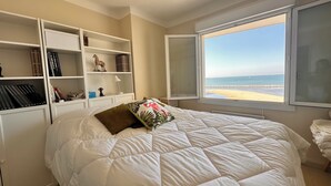 Un dormitorio con una cama grande, una ventana con vista a la playa y estanterías empotradas con libros y objetos decorativos.