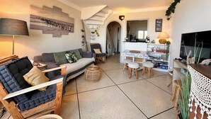 Una sala de estar acogedora con un sofá, una mesa de comedor con sillas, un televisor y una cocina al fondo.
