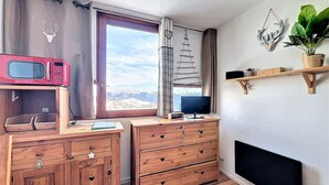 A cozy room with a wooden dresser, a microwave, a TV, and a window with a view of mountains. - 50m from ski slopes, 14th floor, swimming pool, tv, ski locker, 16m², Le Corbier (Le Corbier)