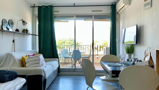 A room with a bed, a desk with chairs, a TV, and a balcony with a view.