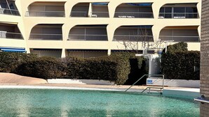 A pool area with a clear view of a building with multiple balconies and a sign reading "DOUCHE OBLIGATIRE".