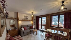 Een gezellige woonkamer met een bank, een eettafel met stoelen en een groot raam met gordijnen.