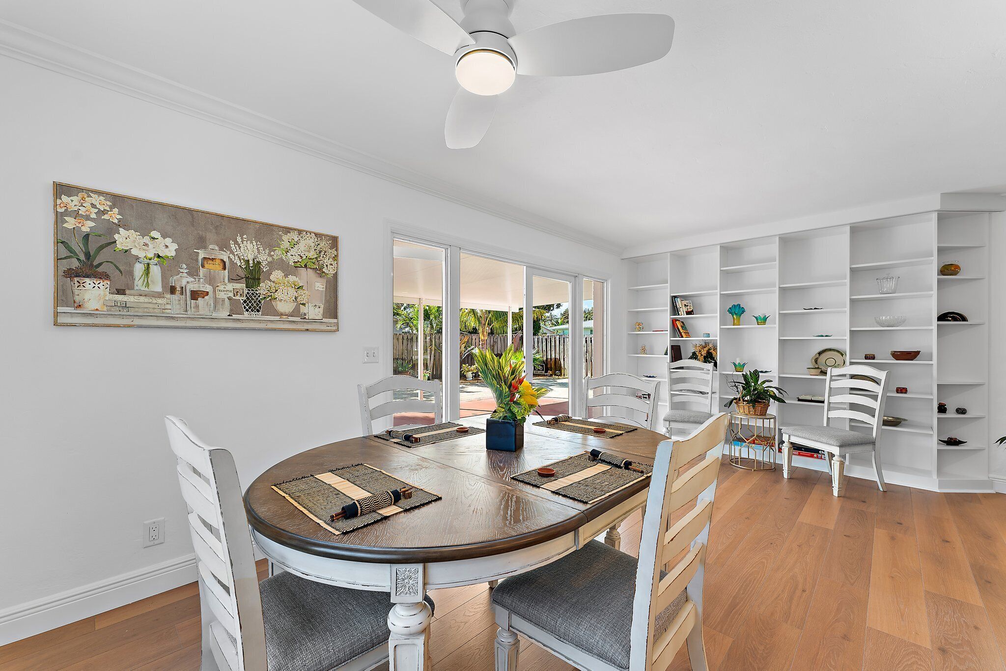 A dining area with a round table, white chairs, and a ceiling fan.