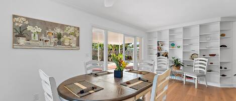 A dining area with a round table, white chairs, and a ceiling fan.