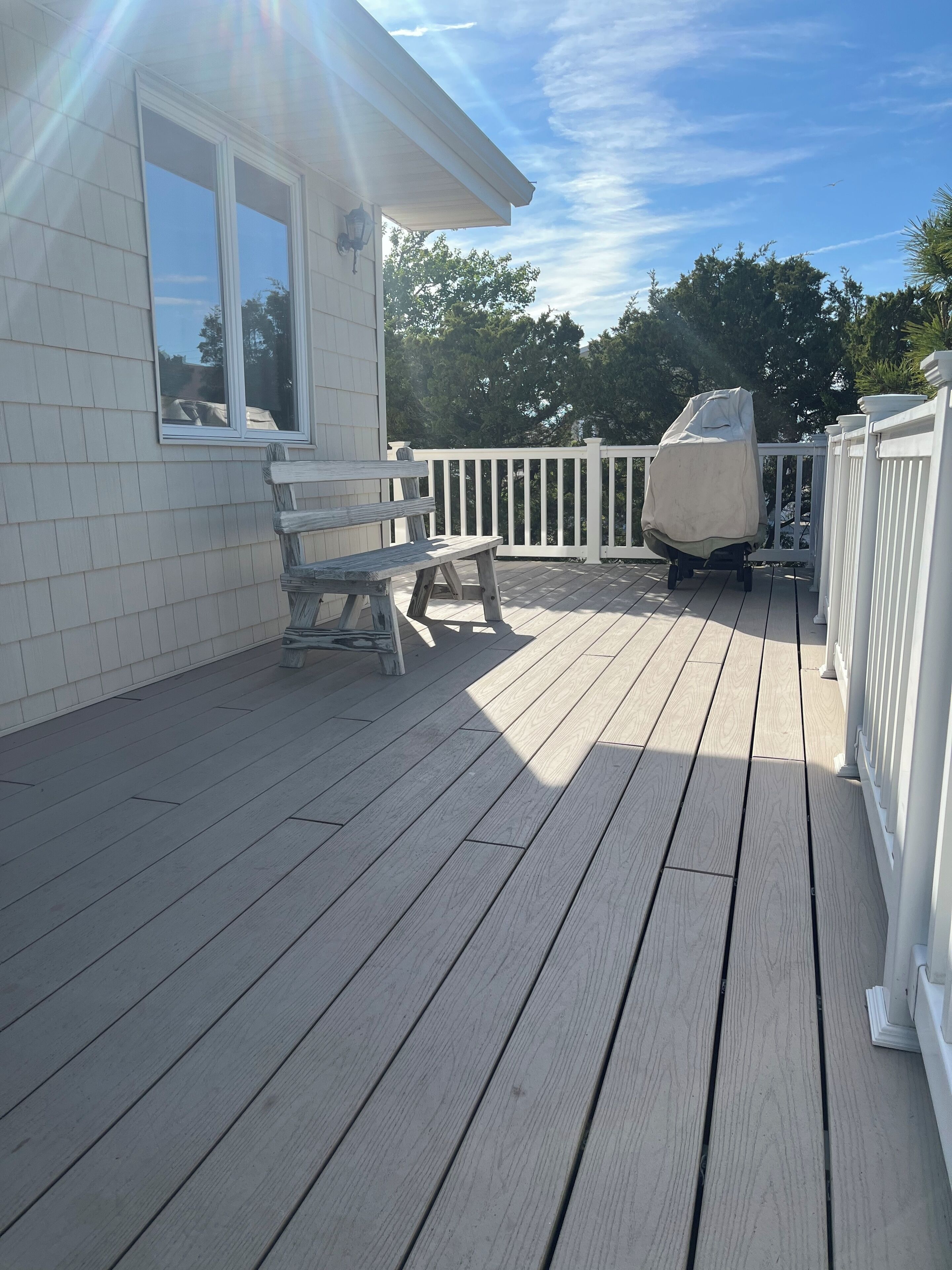 A wooden deck with a white railing, a covered grill, and a bench.
