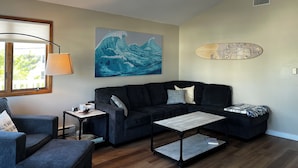 A living room with a black sofa, a coffee table, a lamp, a painting, and a surfboard decoration. -  Newly Renovated 3-Bedroom House in Surf City - Pet Friendly (Surf City)
