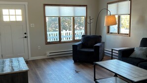A spacious living room with a high ceiling, a ceiling fan, a large window with blinds, a wooden coffee table, a sofa, and a chair. -  Newly Renovated 3-Bedroom House in Surf City - Pet Friendly (Surf City)