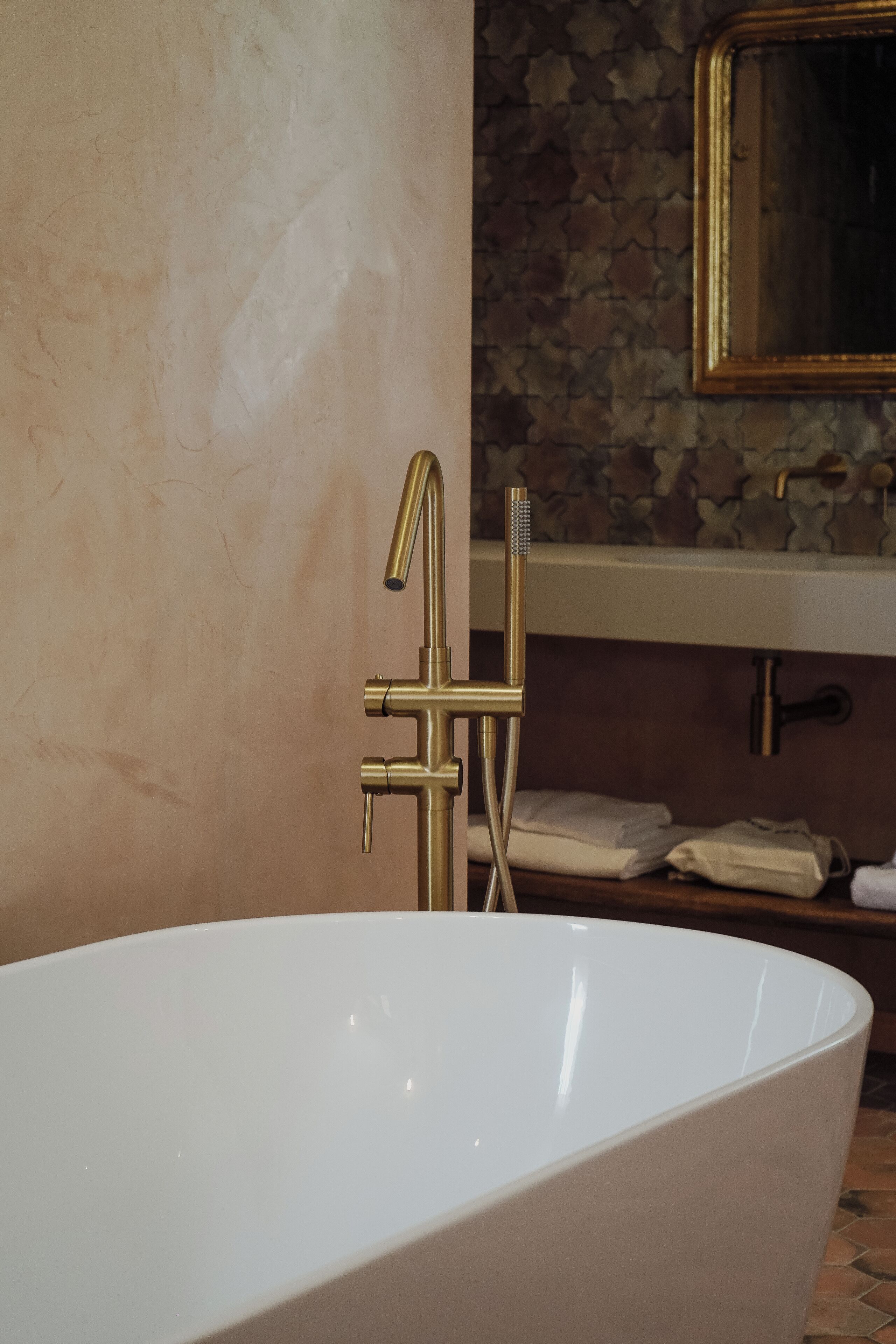 A modern bathroom with a freestanding bathtub, a gold faucet, and a stone-patterned wall.