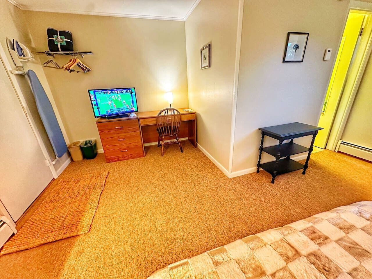 Ein kleines, ordentlich eingerichtetes Schlafzimmer mit einem Bett, einem Schreibtisch mit Stuhl, einem Fernseher und einem kleinen Tisch.