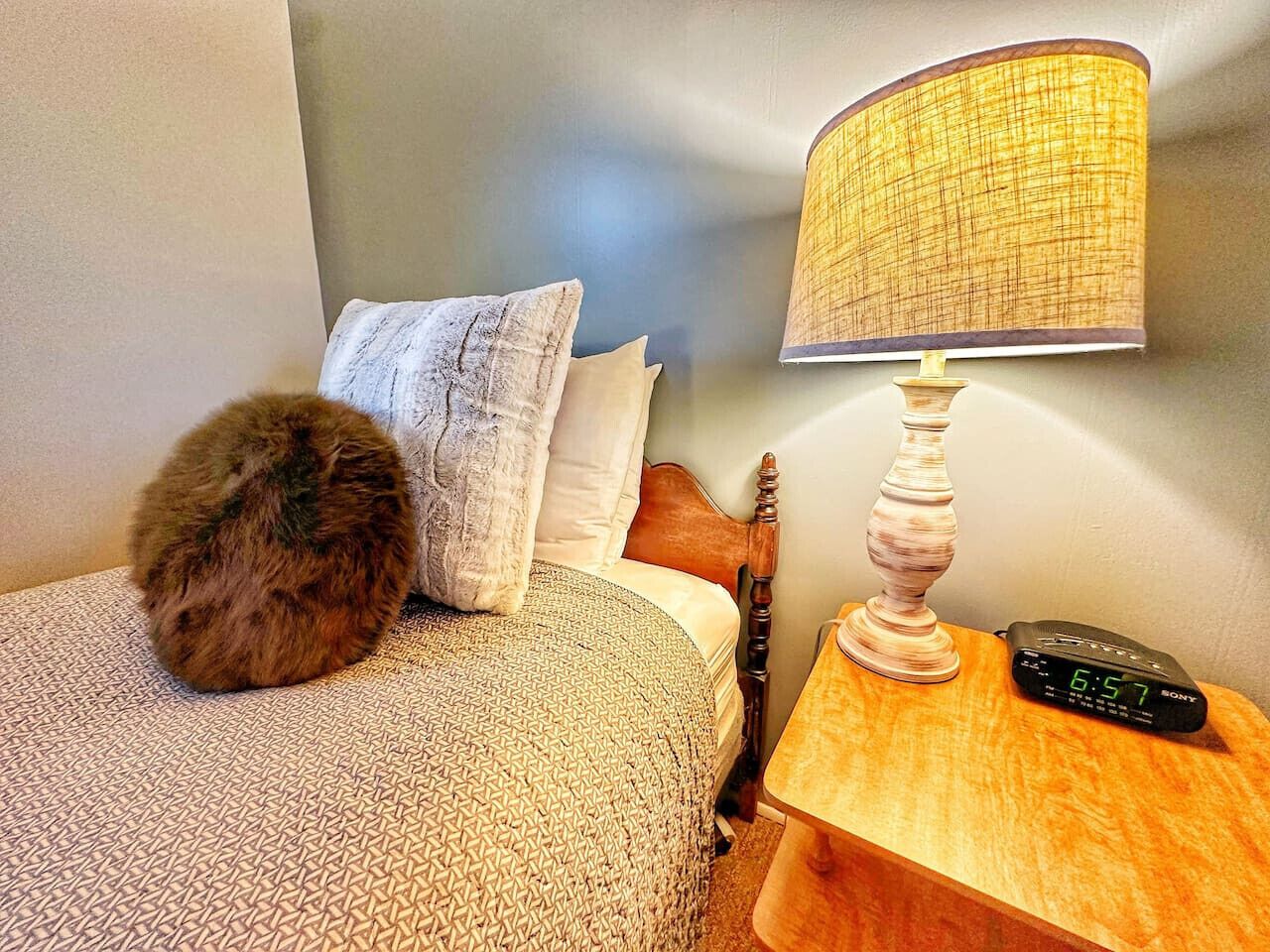 A neatly made bed with patterned bedding, a fluffy pillow, a bedside lamp, and a Sony remote control on a wooden nightstand.