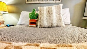 A bed with a textured blanket, a cactus-shaped pillow, and a decorative wooden headboard. - Room 4 - Prickly Pear double room (Manchester)