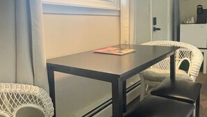 A room with a table and two chairs, a window with curtains, and a lamp. - Room 7 - family room sleeps 4 (Manchester)