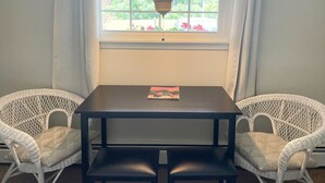 A room with a table and two wicker chairs, a window with a view of greenery, and a hanging lamp. - Room 7 - family room sleeps 4 (Manchester)