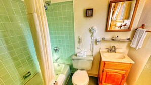 A bathroom with a green tiled shower, a white toilet, a sink with a vanity, and a mirror. - Room 7 - family room sleeps 4 (Manchester)