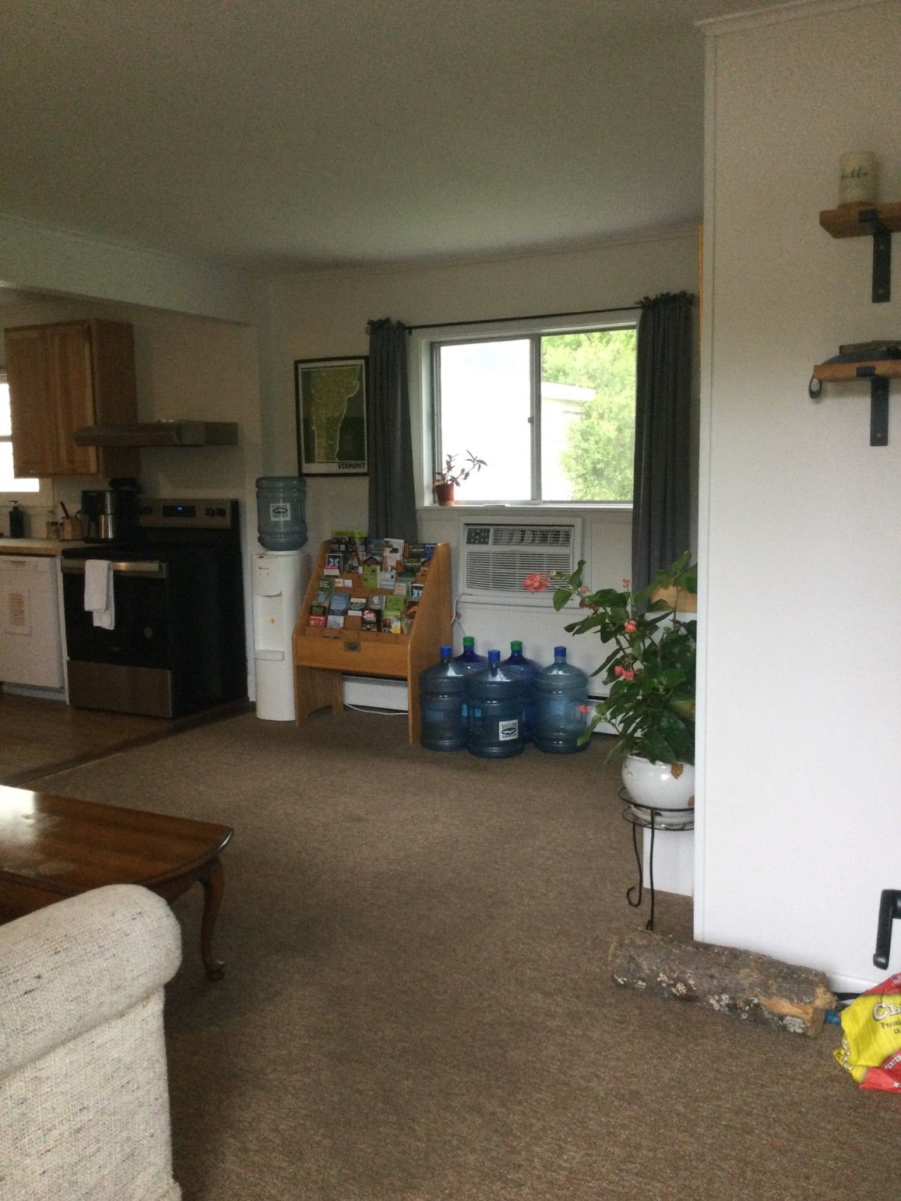 A kitchen with a refrigerator, stove, and a water dispenser. There are large water jugs and a potted plant near the window.