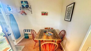 A dining area with a wooden table and four chairs, a small shelf with towels, and a framed picture on the wall. - Cloud 9 family double sleeps 4 (Manchester)