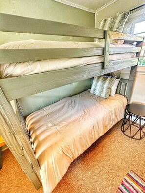 Ein Etagenbett mit einem Einzelbett oben und einem Bett unten, ein kleiner runder Tisch und ein farbenfroher Teppich.