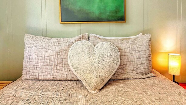 A bedroom with a bed, a heart-shaped pillow, and a framed artwork of a cloud on the wall. - Cloud 9 family double sleeps 4 (Manchester)