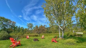 A grassy outdoor area with several red Adirondack chairs and a fire pit. - Zen 10, relax and retreat in the heart of Vermont (Manchester)