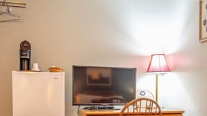 A compact room with a wooden desk, a chair, a television, a small refrigerator, and a lamp. - Alpine 5, cozy Vermont retreat (Manchester)