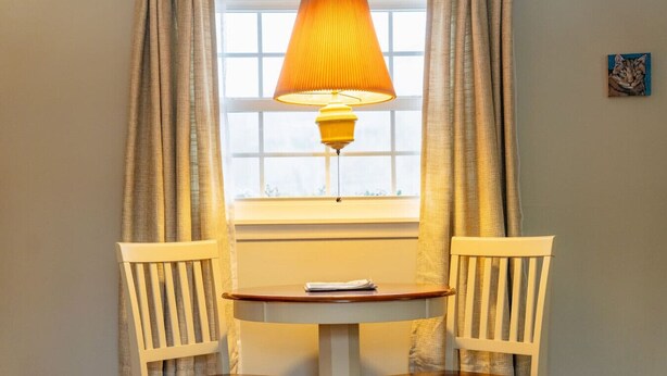 A small room with a table and two chairs, a window with curtains, and a lamp on the table. - Alpine 5, cozy Vermont retreat (Manchester)