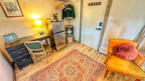 A compact room with a desk, chair, refrigerator, and a small rug.