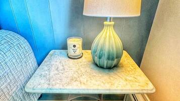 A small bedside table with a lamp, a candle, and a container of vanilla bean candles.