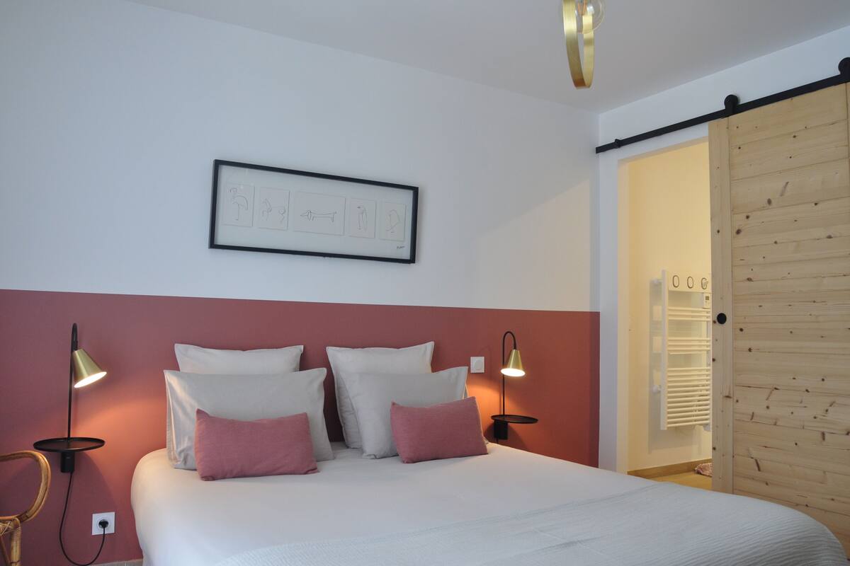 Ein Schlafzimmer mit einem Bett, zwei Wandleuchten, einem gerahmten Bild und einer Holztür.