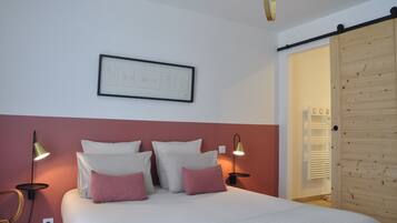 Un dormitorio con una cama, dos lámparas de pared, un cuadro enmarcado y una puerta de madera.