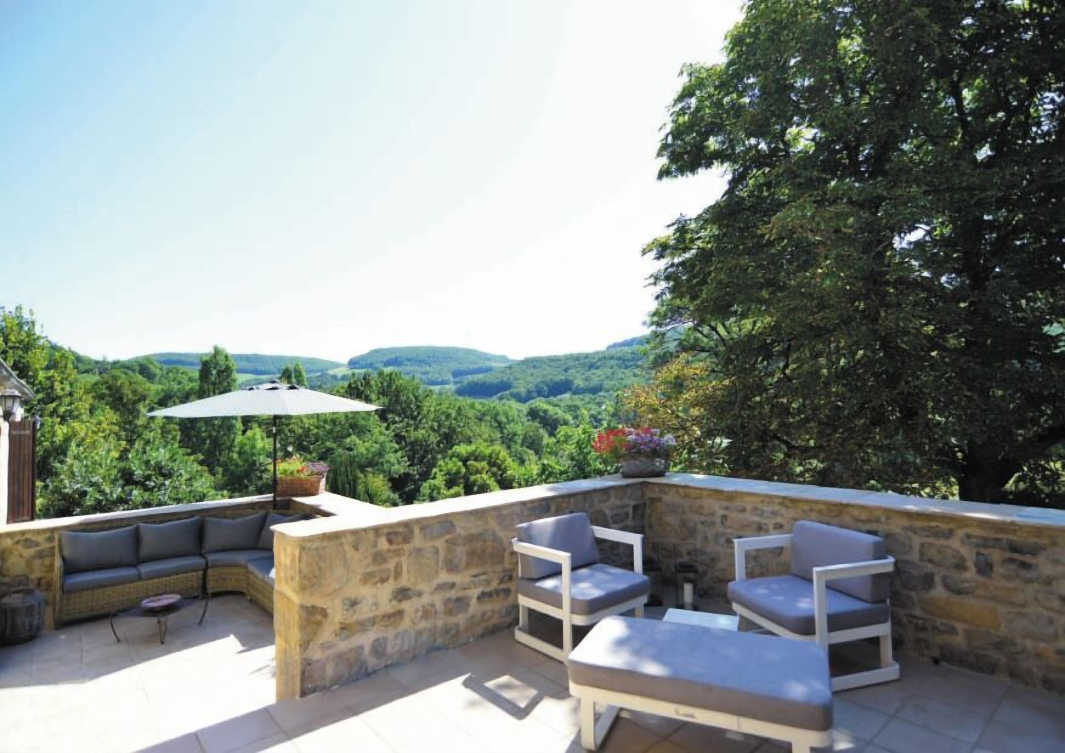Une terrasse en pierre avec des sièges d’extérieur, une table et un parasol.