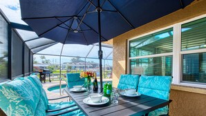 Eine überdachte Terrasse mit Tisch für zwei Personen, blauen Sitzmöbeln mit Muster und Blick ins Grüne.