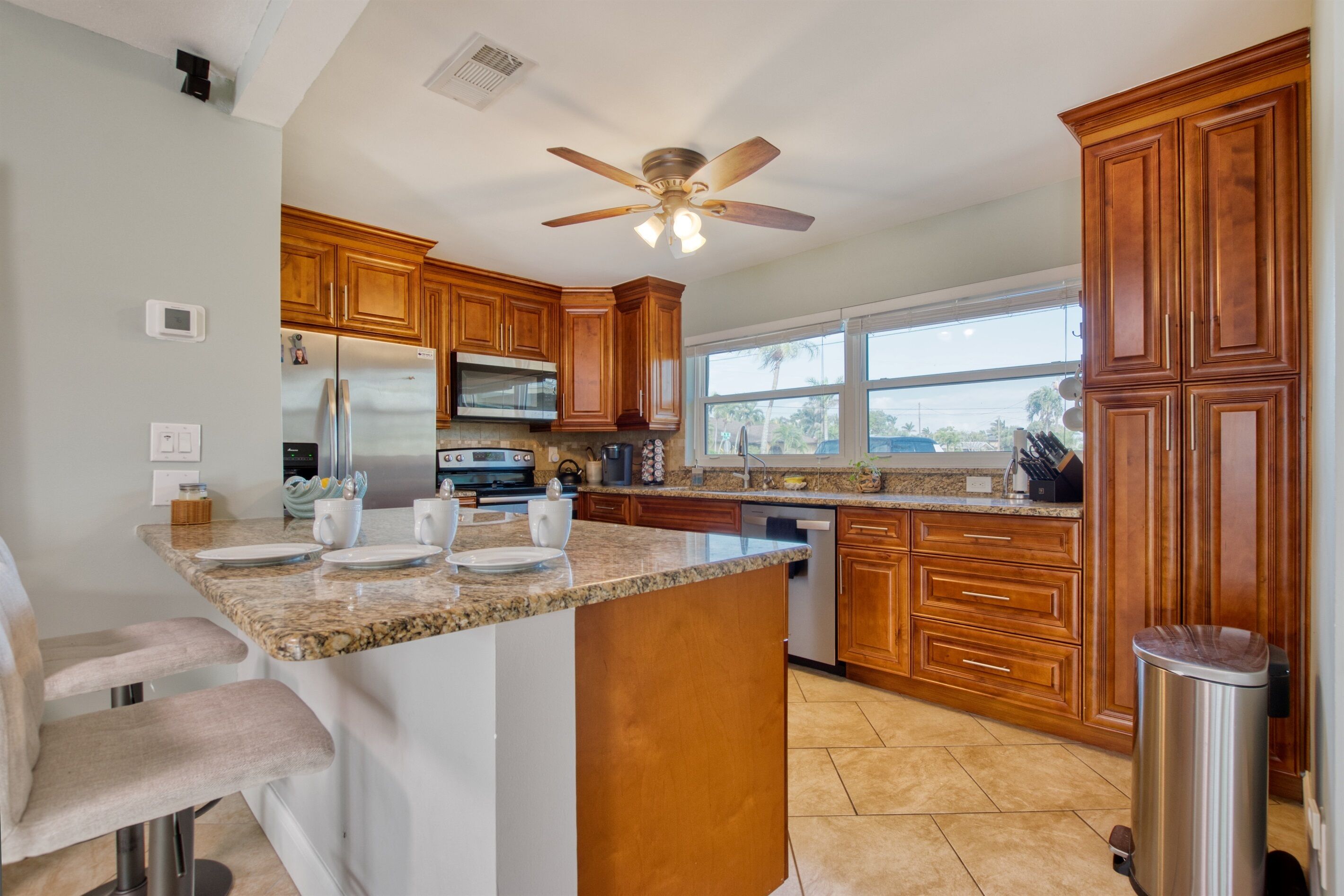 A modern kitchen with wooden cabinets, a granite countertop, stainless steel appliances, and a large window.