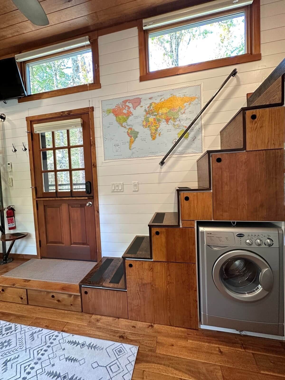 A wooden staircase with a washing machine, a world map, and a door with a window.