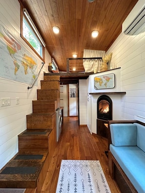 A compact interior with a wooden staircase, a fireplace, a sofa, and a world map on the wall.