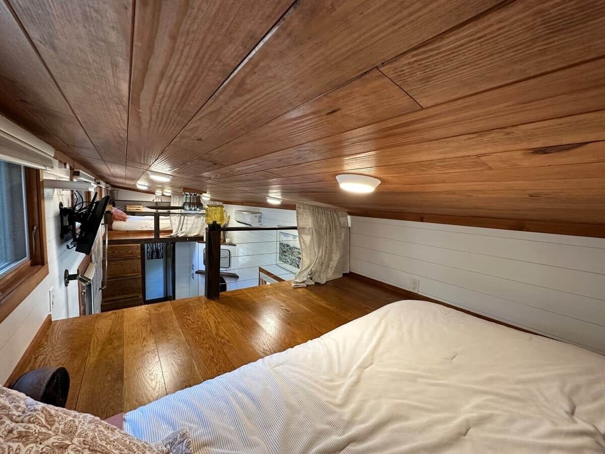 A compact room with a bed, wooden flooring, a kitchenette, and a small window.