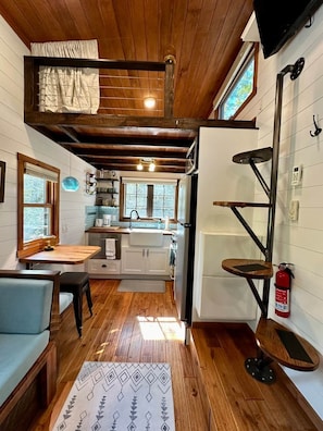 A compact kitchen with a wooden ceiling, a dining area with a table and chairs, and a small seating area with a sofa. - New Listing! AmongstTheAspens - Off-Grid Tiny Home (Saco)