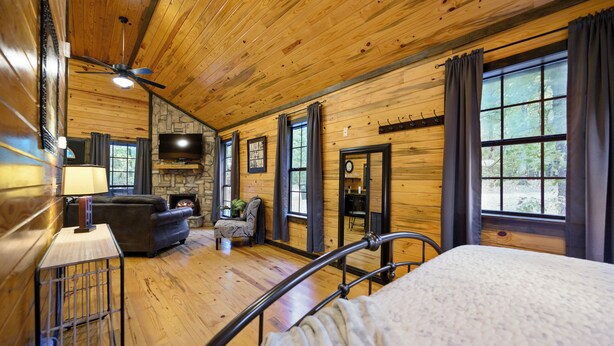 A log cabin interior with a bed, a fireplace, a television, and a stone wall. - Jax Ridge-Studio 1 Bedroom (Broken Bow)