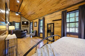 A log cabin interior with a bed, a fireplace, a television, and a stone wall. - Jax Ridge-Studio 1 Bedroom (Broken Bow)