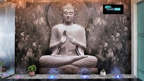 A large Buddha statue in a meditative pose, set against a textured wall with a logo and slogan. - Hotel Bramha inn (Pune)